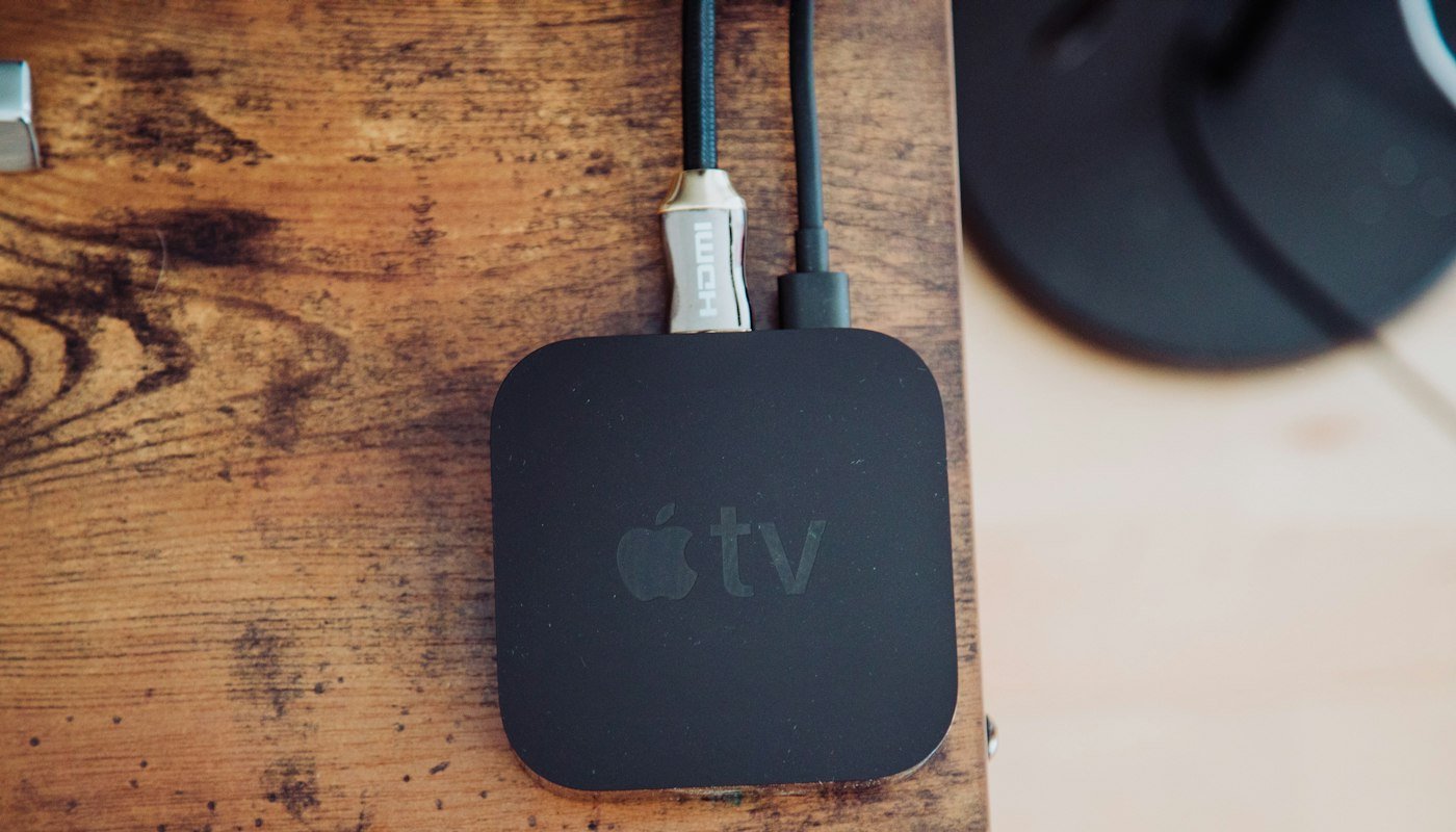 Een zwart Apple TV-kastje op een houten tafel met de HDMI-kabel en stroomkabel aangesloten