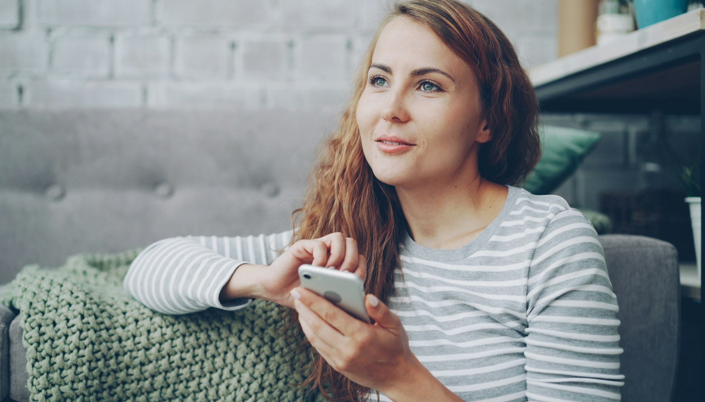 Een vrouw op de bank met een smartphone in haar hand kijkt op naar het scherm